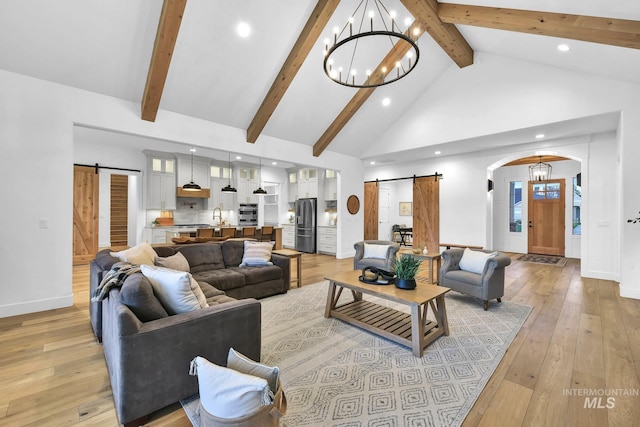 living room featuring a barn door, a chandelier, high vaulted ceiling, beam ceiling, and light wood-style floors