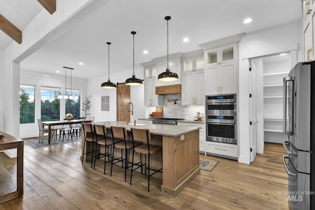 kitchen featuring appliances with stainless steel finishes, tasteful backsplash, a kitchen breakfast bar, light wood-style flooring, and white cabinetry