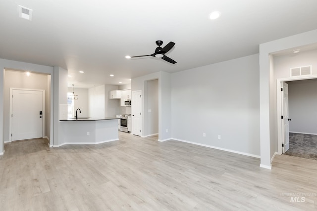 unfurnished living room featuring light wood-style floors, visible vents, a sink, and ceiling fan