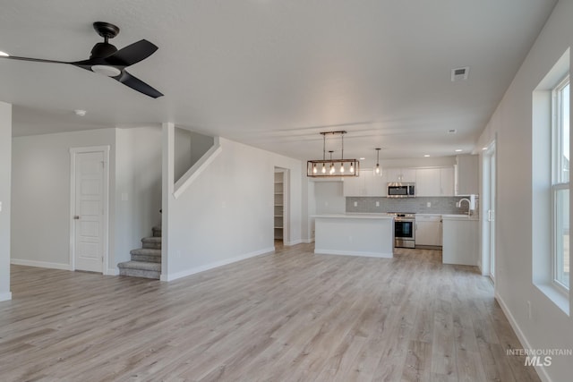 unfurnished living room with visible vents, a ceiling fan, a sink, light wood-type flooring, and stairs