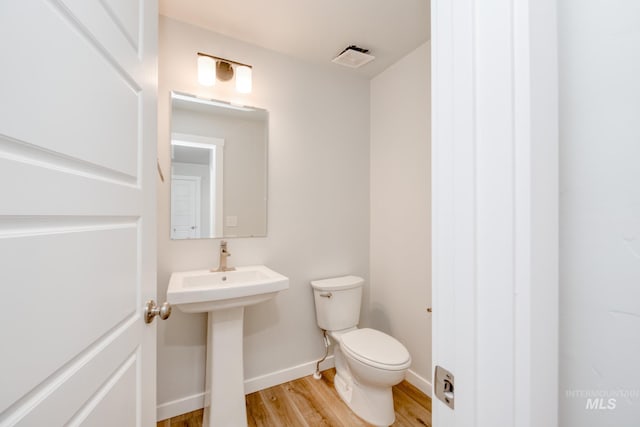 bathroom featuring a sink, toilet, visible vents, baseboards, and wood finished floors