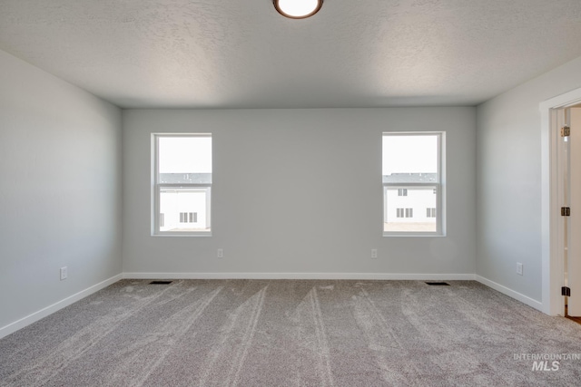 carpeted empty room featuring a textured ceiling, a wealth of natural light, and visible vents
