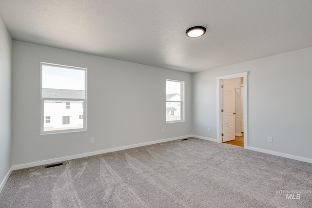 unfurnished room with baseboards, carpet floors, visible vents, and a wealth of natural light