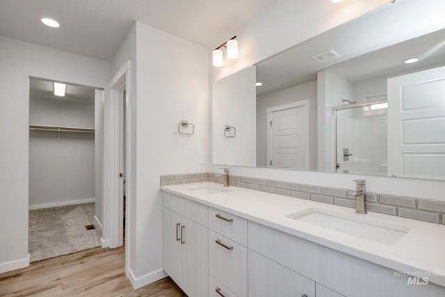 bathroom featuring double vanity, a shower stall, wood finished floors, and a sink