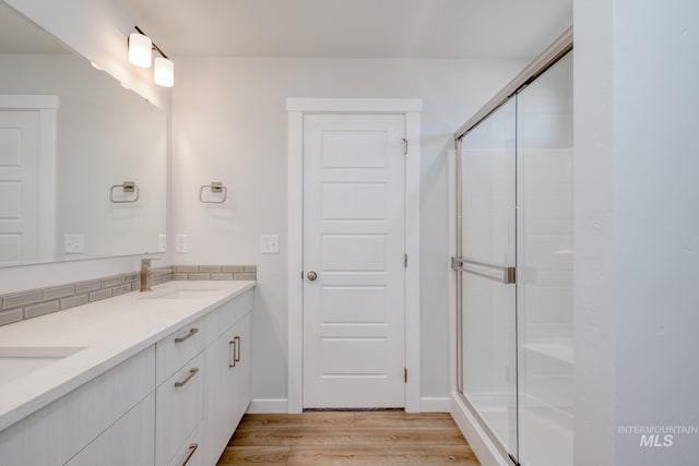 bathroom with a shower stall, wood finished floors, double vanity, and a sink