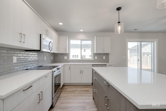kitchen featuring a sink, stainless steel microwave, tasteful backsplash, electric range oven, and light wood-style flooring