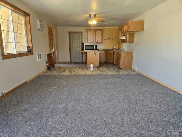 kitchen featuring ceiling fan, a center island, light colored carpet, and sink