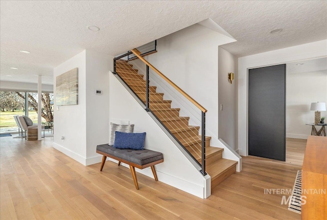 stairway featuring a textured ceiling, baseboards, and wood finished floors