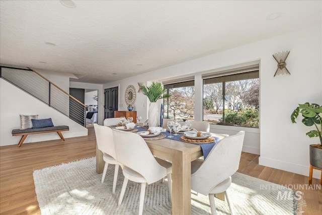 dining space featuring stairway, wood finished floors, baseboards, and a textured ceiling