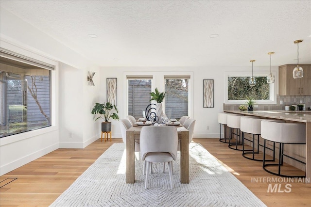 dining space featuring a wealth of natural light, light wood-style flooring, a textured ceiling, and baseboards