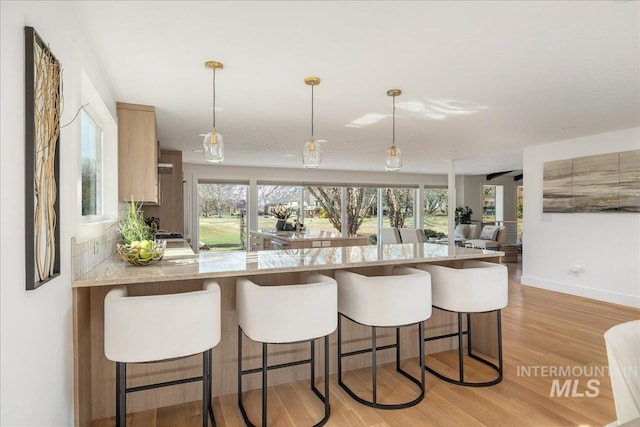 kitchen featuring a breakfast bar, light stone counters, light wood-style floors, and baseboards