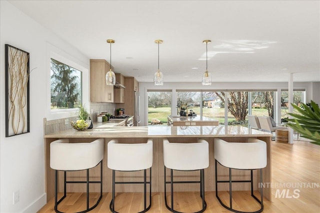 kitchen with light wood-style floors, backsplash, a healthy amount of sunlight, and a peninsula