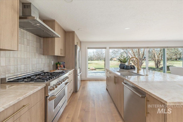 kitchen featuring light wood-type flooring, light brown cabinets, a sink, appliances with stainless steel finishes, and wall chimney exhaust hood