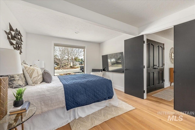 bedroom with beam ceiling, a textured ceiling, and light wood finished floors