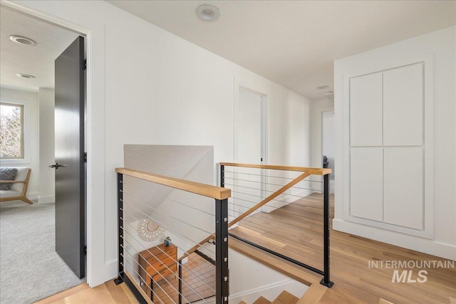 hallway featuring light carpet, an upstairs landing, light wood-style floors, and baseboards