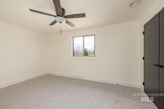 carpeted empty room featuring baseboards and a ceiling fan