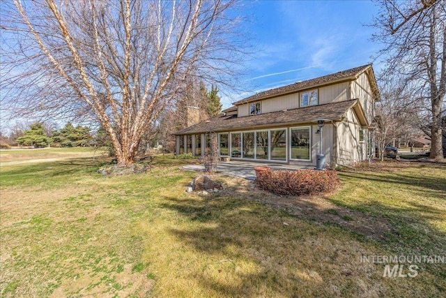 rear view of property featuring a yard, a patio, and a chimney