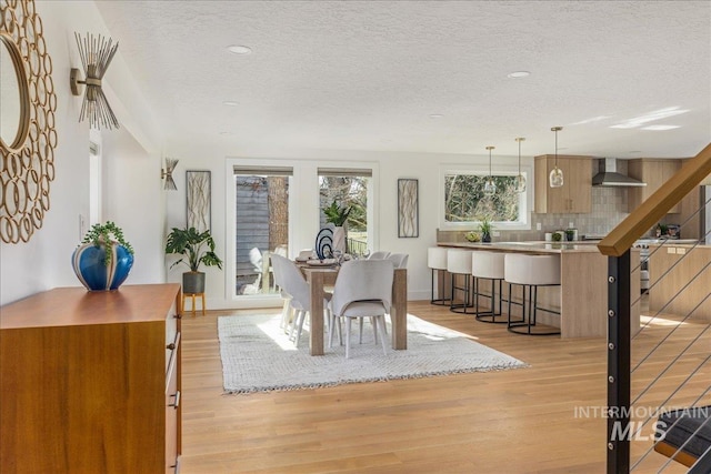 dining area with light wood-style flooring, a textured ceiling, and baseboards