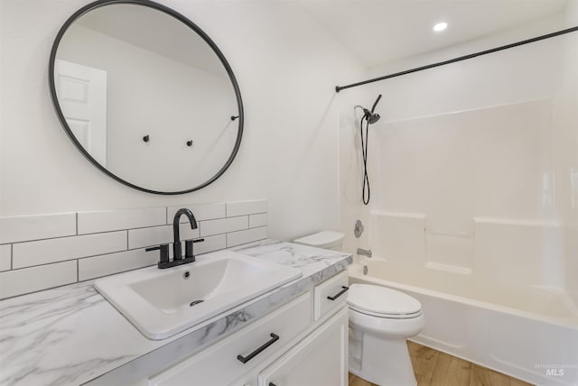 full bath with toilet, wood finished floors, vanity, tasteful backsplash, and washtub / shower combination