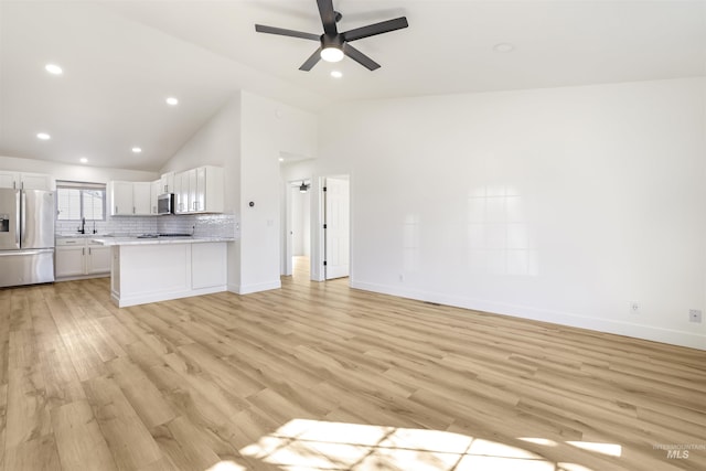 unfurnished living room with baseboards, a ceiling fan, vaulted ceiling, light wood-type flooring, and a sink