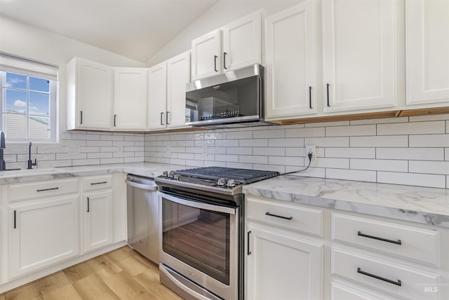 kitchen with lofted ceiling, appliances with stainless steel finishes, light wood-style floors, white cabinets, and a sink