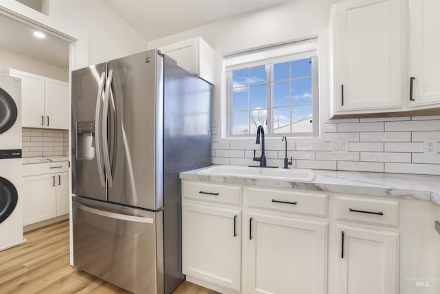 kitchen featuring a sink, stainless steel fridge, white cabinetry, and stacked washer / drying machine