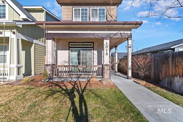 entrance to property featuring a porch, fence, board and batten siding, and a lawn