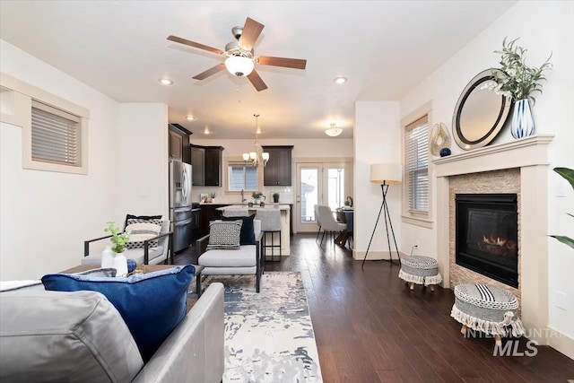 living area featuring ceiling fan with notable chandelier, a glass covered fireplace, dark wood-style floors, recessed lighting, and baseboards