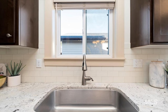 details featuring dark brown cabinetry, backsplash, light stone countertops, and a sink