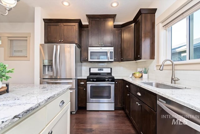 kitchen with light stone counters, a sink, dark wood-type flooring, appliances with stainless steel finishes, and backsplash