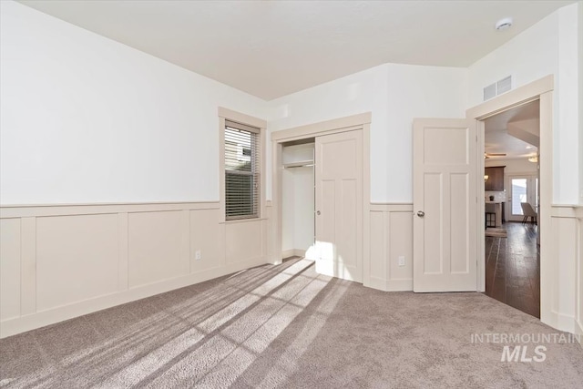 unfurnished bedroom with visible vents, a closet, a decorative wall, wainscoting, and carpet flooring