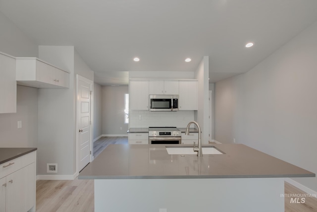 kitchen with sink, tasteful backsplash, appliances with stainless steel finishes, an island with sink, and white cabinets