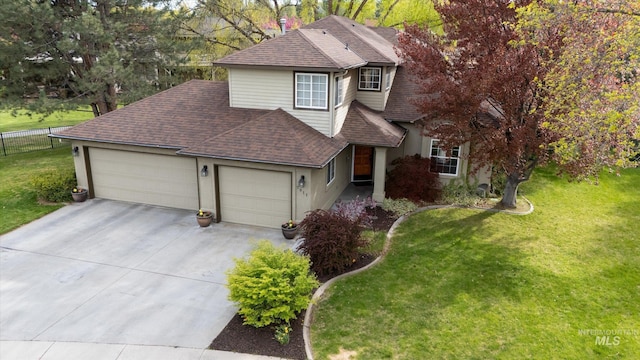 traditional home with concrete driveway, a front lawn, a shingled roof, an attached garage, and fence