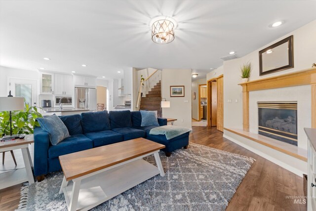 living area featuring a tiled fireplace, wood finished floors, recessed lighting, and stairway