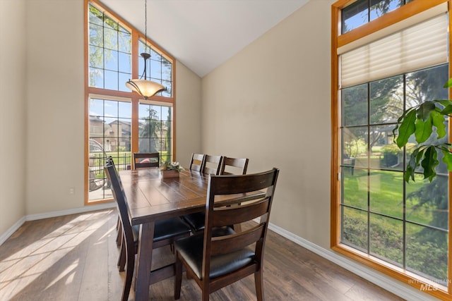 dining space featuring dark wood-type flooring, high vaulted ceiling, and baseboards