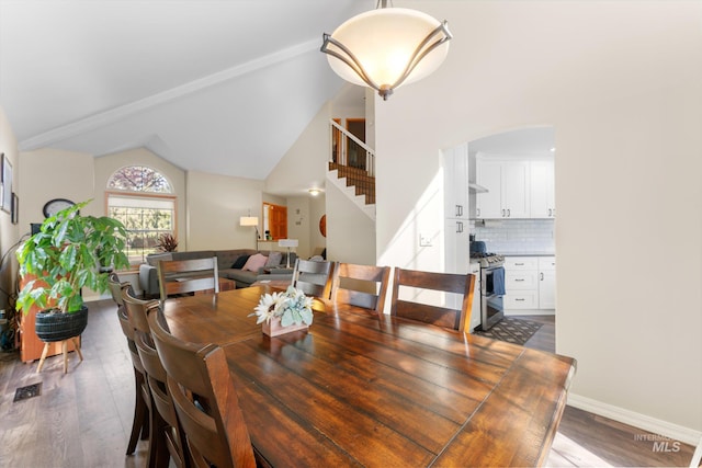 dining room with wood finished floors, stairs, arched walkways, baseboards, and lofted ceiling