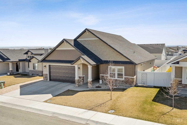 craftsman house with an attached garage, stone siding, fence, a front lawn, and driveway