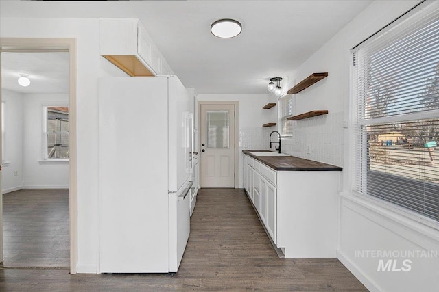 kitchen with a sink, white cabinetry, freestanding refrigerator, open shelves, and dark countertops