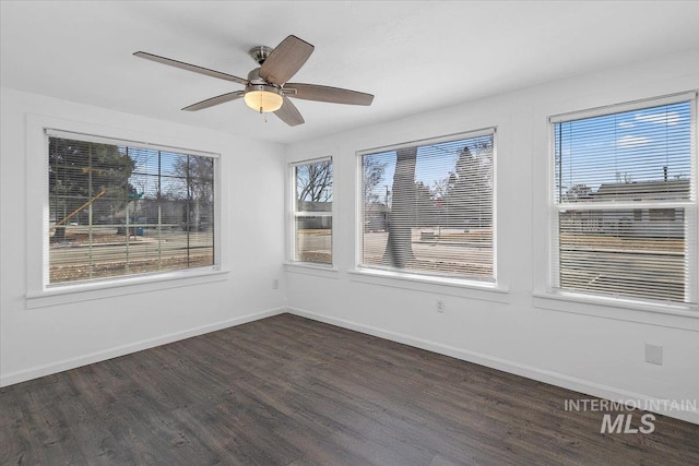 empty room with dark wood-style flooring, a ceiling fan, and baseboards