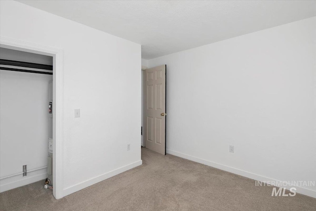 unfurnished bedroom featuring baseboards, a closet, and light colored carpet