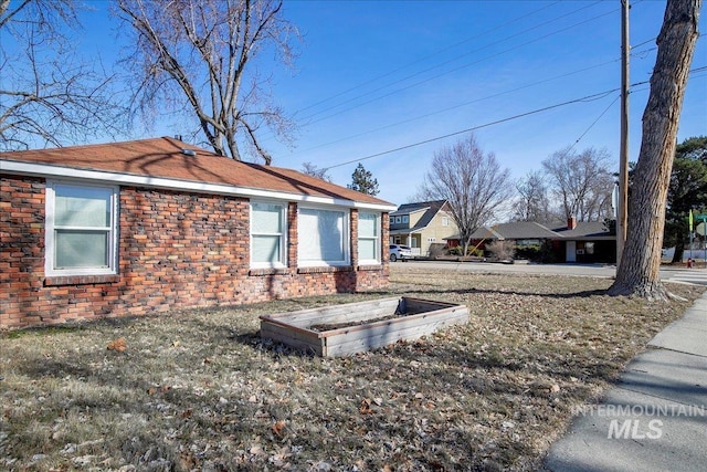 view of side of home with brick siding, a lawn, and a vegetable garden