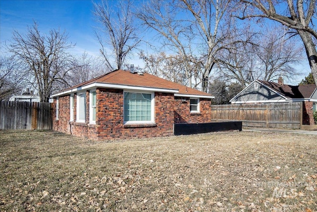 view of property exterior featuring a yard, brick siding, and fence