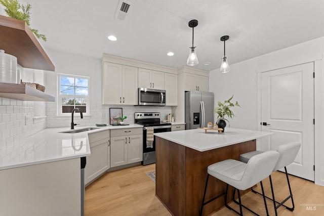 kitchen featuring pendant lighting, sink, appliances with stainless steel finishes, a kitchen island, and white cabinetry