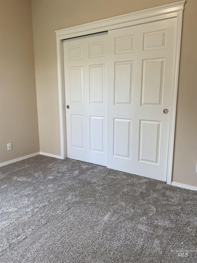 unfurnished bedroom with dark carpet and a closet