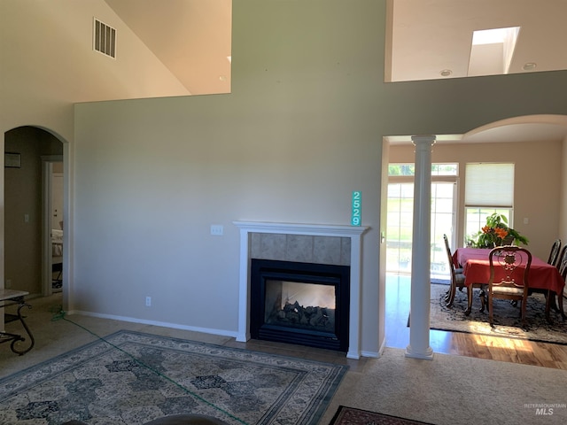 living room featuring decorative columns, a tile fireplace, and a towering ceiling