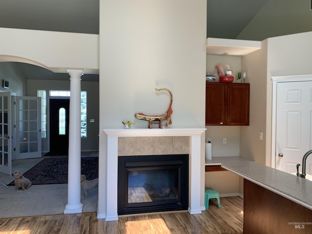 living room featuring vaulted ceiling, a tiled fireplace, decorative columns, and hardwood / wood-style floors