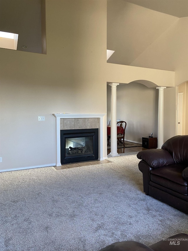 living room featuring a tiled fireplace, high vaulted ceiling, light carpet, and decorative columns