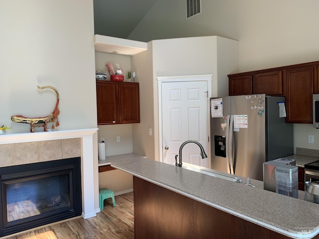 kitchen with appliances with stainless steel finishes, sink, a tiled fireplace, kitchen peninsula, and light hardwood / wood-style flooring