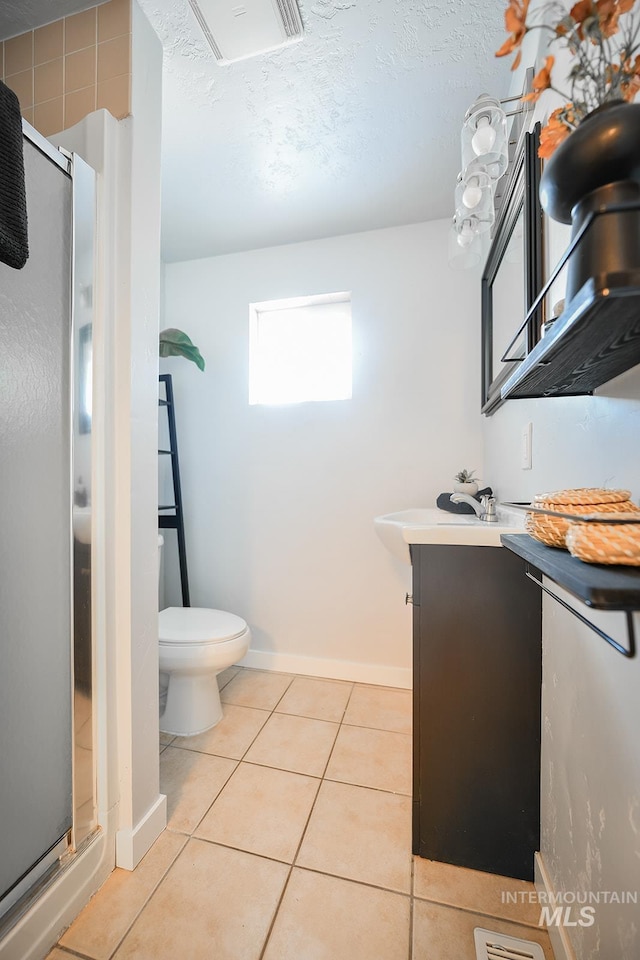 bathroom featuring toilet, vanity, a shower with door, and tile patterned flooring