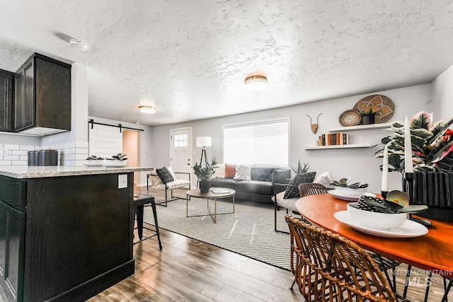 dining area featuring a barn door, a textured ceiling, and dark hardwood / wood-style flooring